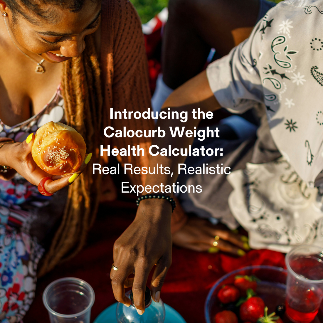 A lifestyle image of two people enjoying food outdoors on a picnic blanket, with one person holding a bread roll and another reaching for a drink.